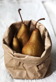 three pears in a paper bag on a bed