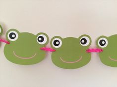 there are three green frogs hanging on the wall with pink ribbon around their necks and eyes