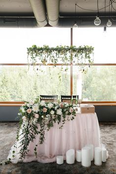 the table is set up with candles and greenery for an elegant wedding reception in front of a large window