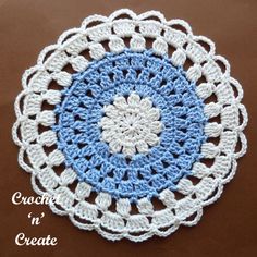 a crocheted doily with blue and white circles on the center, sitting on a brown surface