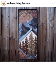 a painting hanging on the side of a wooden fence with trees and mountains painted on it