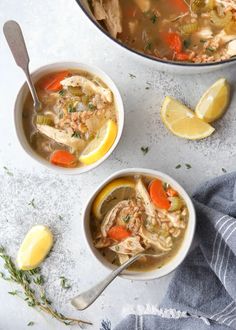 two bowls of chicken soup with lemons, carrots and parsley on the side