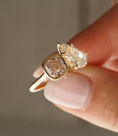 a woman's hand is holding an engagement ring with two pear shaped diamonds on it