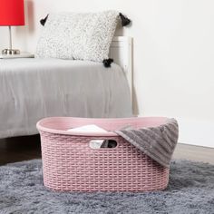 a pink basket sitting on top of a rug next to a bed with a gray blanket