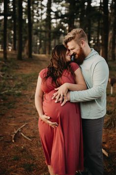 a pregnant couple cuddle in the woods