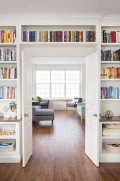 a living room filled with lots of books on top of white bookcases next to a window