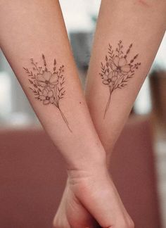 two people holding hands with matching tattoos on their arms and the other hand has flowers in it