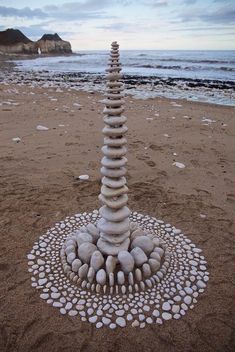 a sculpture made out of rocks sitting on top of a sandy beach next to the ocean