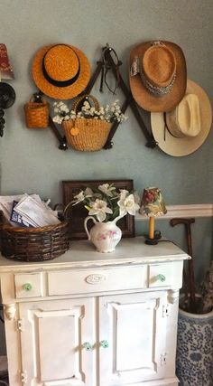 a white dresser topped with lots of hats next to a wall filled with other items