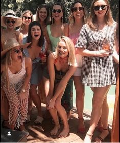 a group of women standing next to each other in front of a pool with drinks