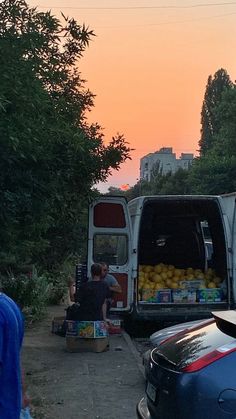 a man sitting in the back of a van next to a truck filled with fruit