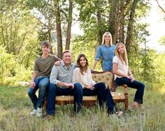 a family sitting on a bench in the middle of a field with trees behind them