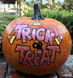 a large pumpkin with the words trick and treat painted on it's side in front of some bushes