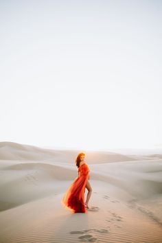 a woman in an orange dress walking through the desert