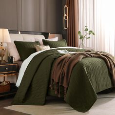 a bed with green comforter and pillows in a room next to a lamp on a table