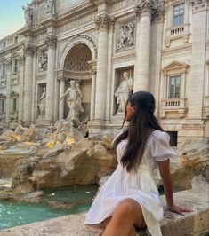 a woman in white dress sitting on ledge next to water