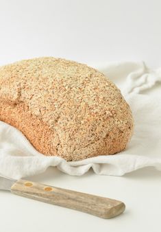 a loaf of bread sitting on top of a white cloth next to a wooden knife