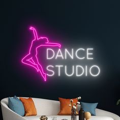 a neon sign that says dance studio on the wall above a white couch with pillows