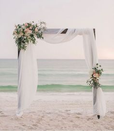 a wedding arch with flowers and greenery on the sand at the beach in front of the ocean