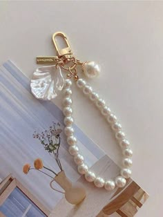 a white pearl necklace with a gold keychain on top of it and a vase in the background