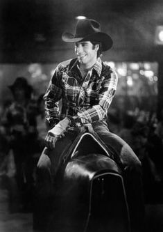 a black and white photo of a man on a horse wearing a cowboy hat with people in the background