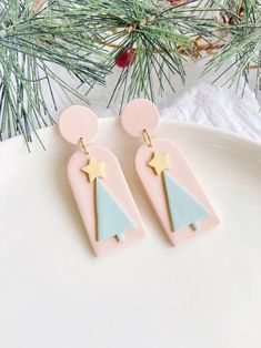 the pink and blue earrings are hanging from a pine tree branch with gold stars on it