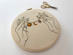 two hands holding sunflowers in front of an embroidery hoop