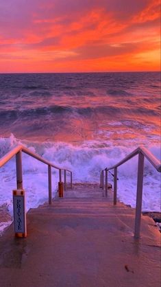 the stairs lead down to the beach as the sun sets over the ocean in the background