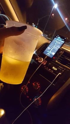 a person is holding a plastic cup filled with liquid in their hand while driving at night