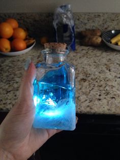 a person holding up a bottle with blue liquid in it and some oranges on the counter