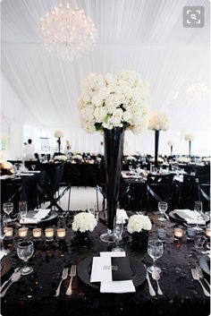 a tall vase filled with white flowers sitting on top of a table covered in black linens