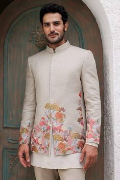 a man standing in front of a wooden door wearing a white suit with colorful flowers on it