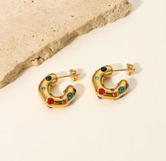 Brighten up your accessory collection with the vibrant Living In Color Earrings. These stunning hoops are adorned with an array of multi-colored stones, adding a splash of color and joy to your ensemble. Perfect for those who love to make a statement, these earrings capture the essence of fun and fashion, making every moment a little more radiant. Crafted with precision, the Living In Color Earrings feature 18K gold-plated stainless steel, ensuring they remain a standout piece in your jewelry bo Multicolor Jeweled Metal Earrings, Multicolor Multi-stone Hoop Earrings As Gift, Trendy Jeweled Earrings For Gift, Multicolor Gemstone Hoop Earrings For Gift, Multicolor Metal Hoop Earrings For Pierced Ears, Ring Necklace, Jewelry Care, Stone Color, Color Splash