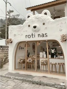 a store front with a white teddy bear on it's side and wooden stools outside