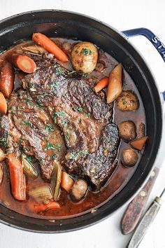 a pot filled with meat and vegetables on top of a white tablecloth next to utensils