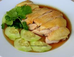 a white plate topped with meat and cucumber slices covered in broth next to sliced celery