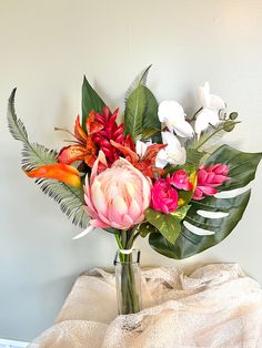 a vase filled with lots of colorful flowers on top of a table next to a white wall