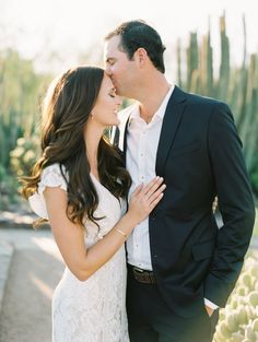 a man and woman kissing in front of cacti