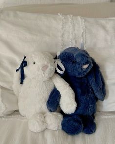 two blue and white stuffed animals sitting next to each other on top of a bed