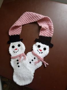 a knitted snowman scarf hanging from a door handle on a brown table with a black hat and pink scarf