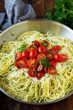 a pan filled with pasta and tomatoes on top of a wooden table next to parsley