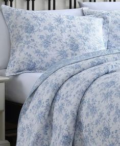 a bed with blue and white comforters on top of it next to a night stand