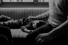 a man laying on top of a couch next to another person sitting in front of a window