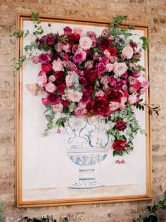 a vase filled with pink and red flowers sitting on top of a table next to a brick wall