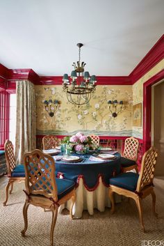 the dining room is decorated with red and gold wallpaper, blue upholstered chairs, and a chandelier