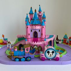 a toy train with mickey mouse on the track in front of a pink princess castle