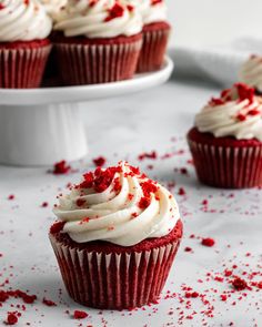 red velvet cupcakes with white frosting and sprinkles on a plate