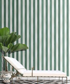 a white chaise lounge chair next to a green striped wall with a potted plant