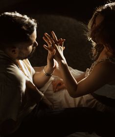 a man and woman sitting on top of a bed holding hands up to each other