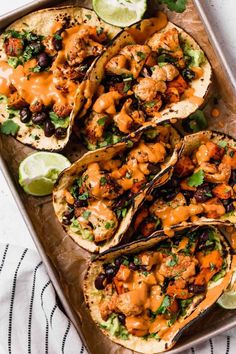 chicken tacos with guacamole and lime wedges on a baking sheet